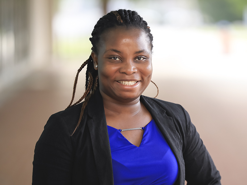 A headshot of Keima Borsuah. Her hair is in long black braids, and she is wearing a blue blouse with a black blazer over it.