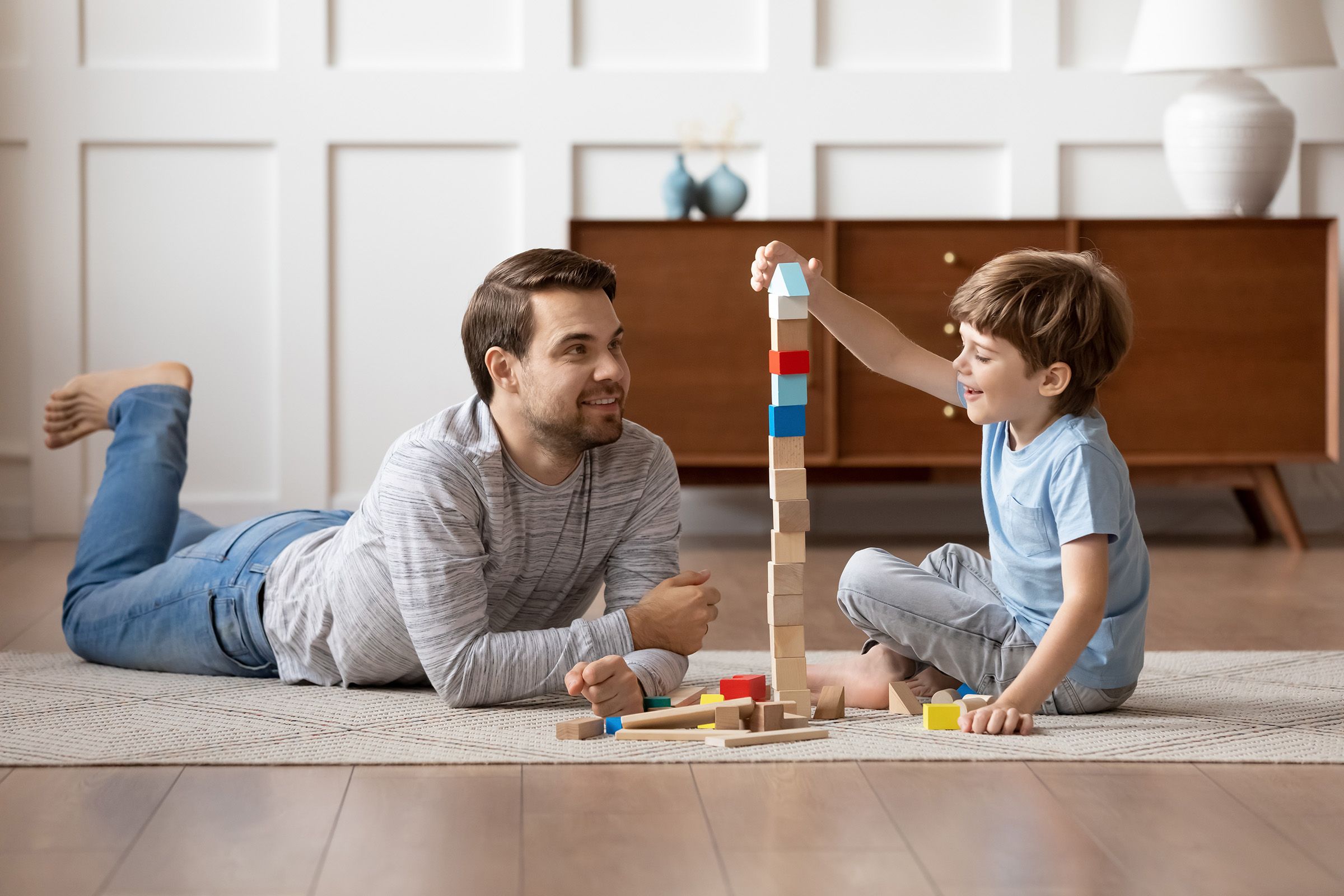 A father and son sitting on the floor playing with building blocks.