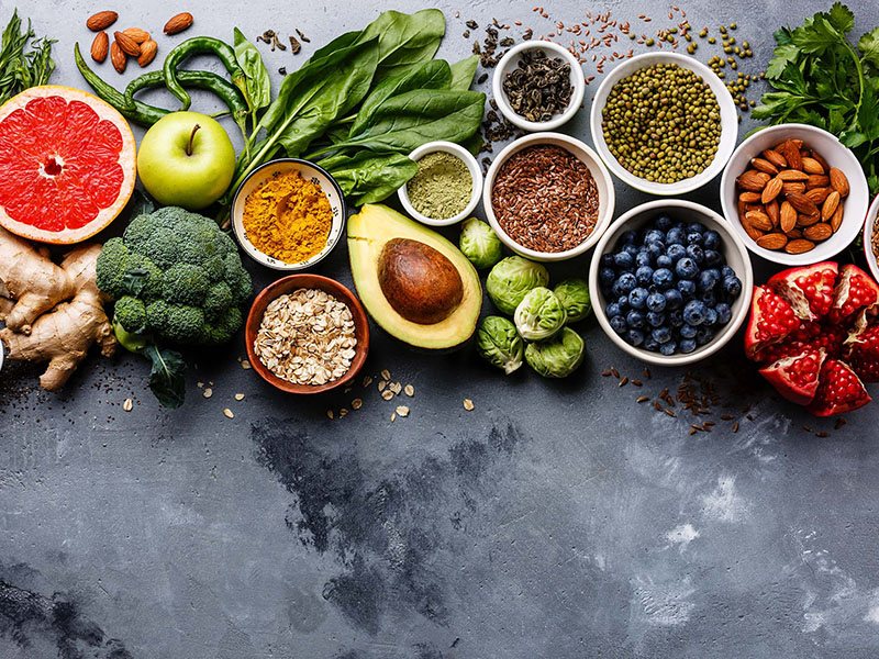 A table of bowls with different kinds of food from berries, grains, powders and nuts with vegetables around it.