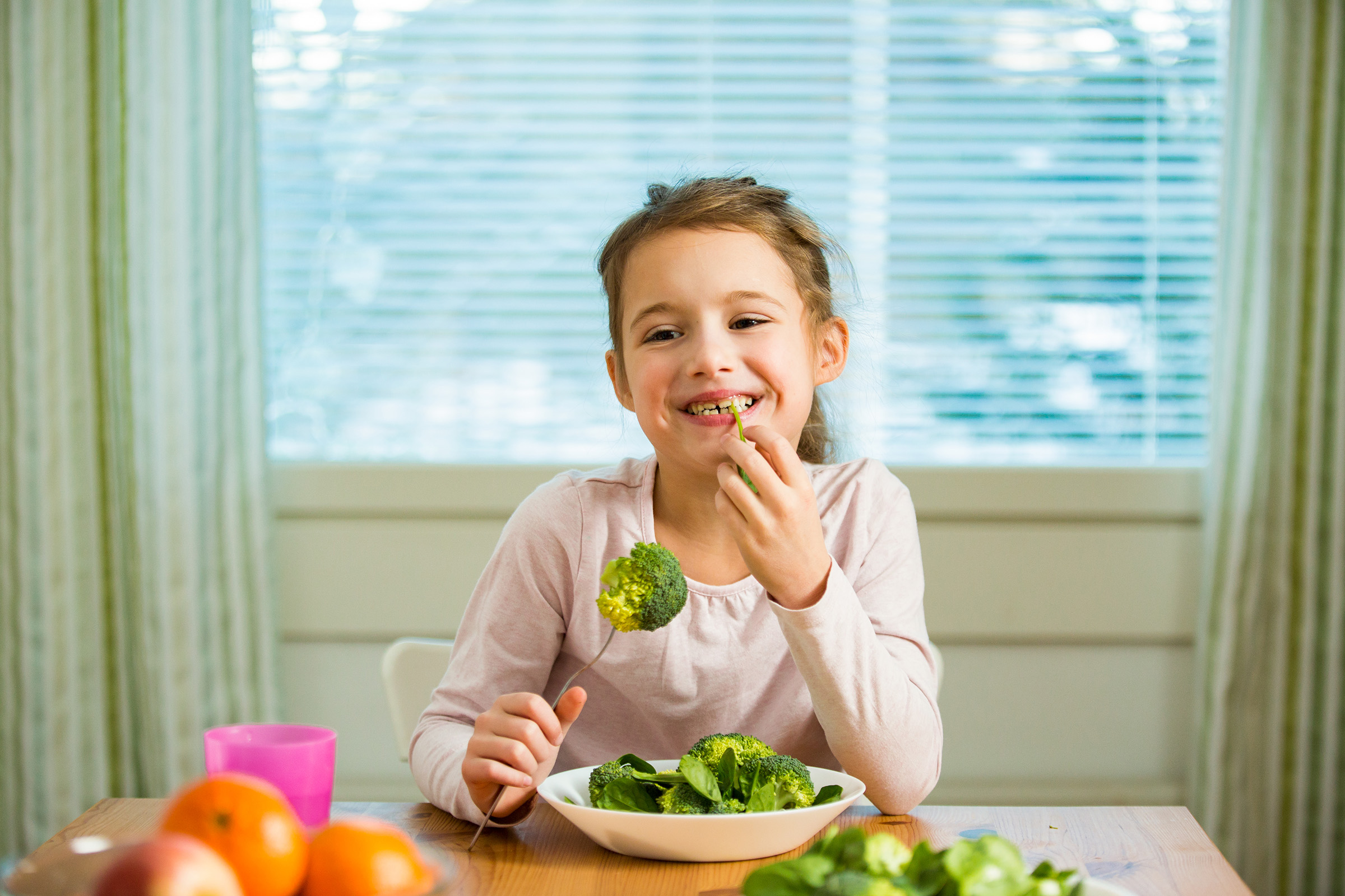 A young girl sitting at a table eating vegetables.