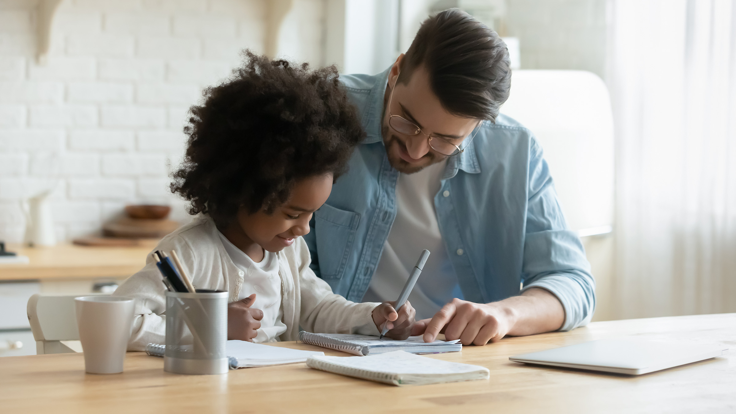 A parent and a child sitting at a table as the parent guides the child through homework.