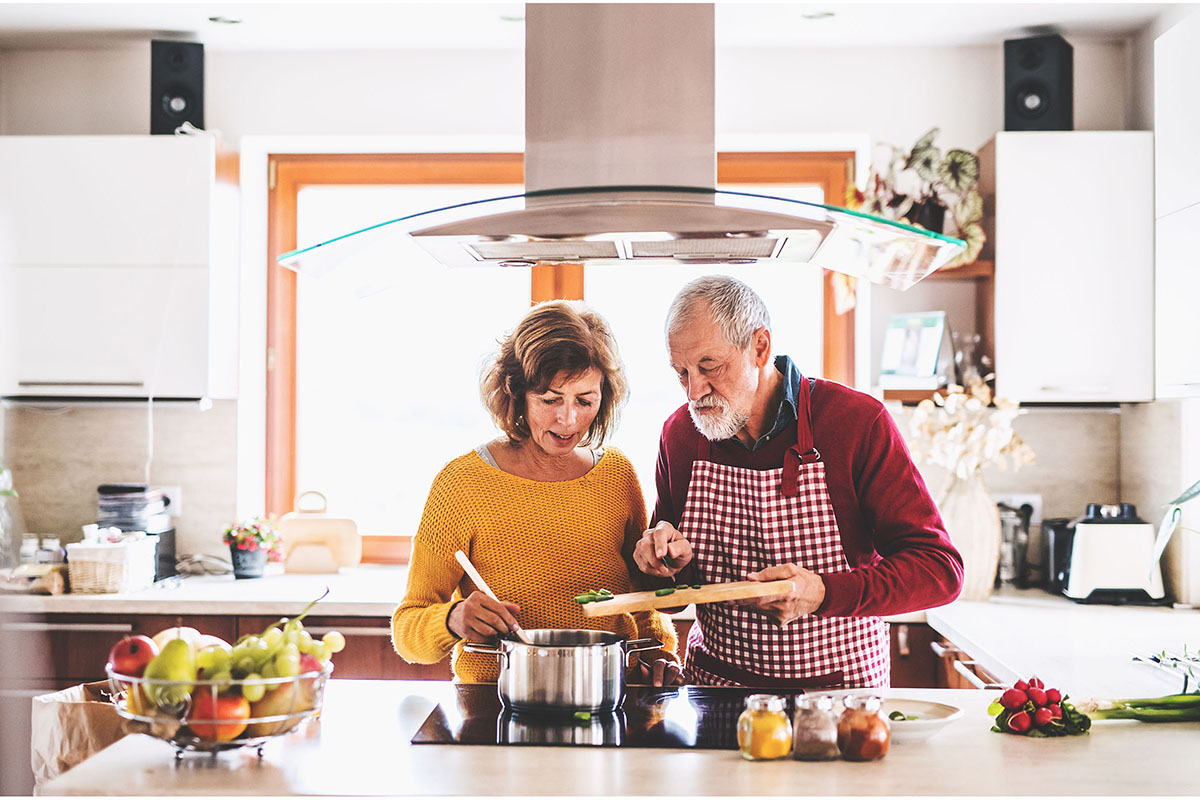 may-2026-cooking-for-one-or-two-1200x800.jpg A man and a woman are standing by the stove, adding ingredients to a cooking pot.