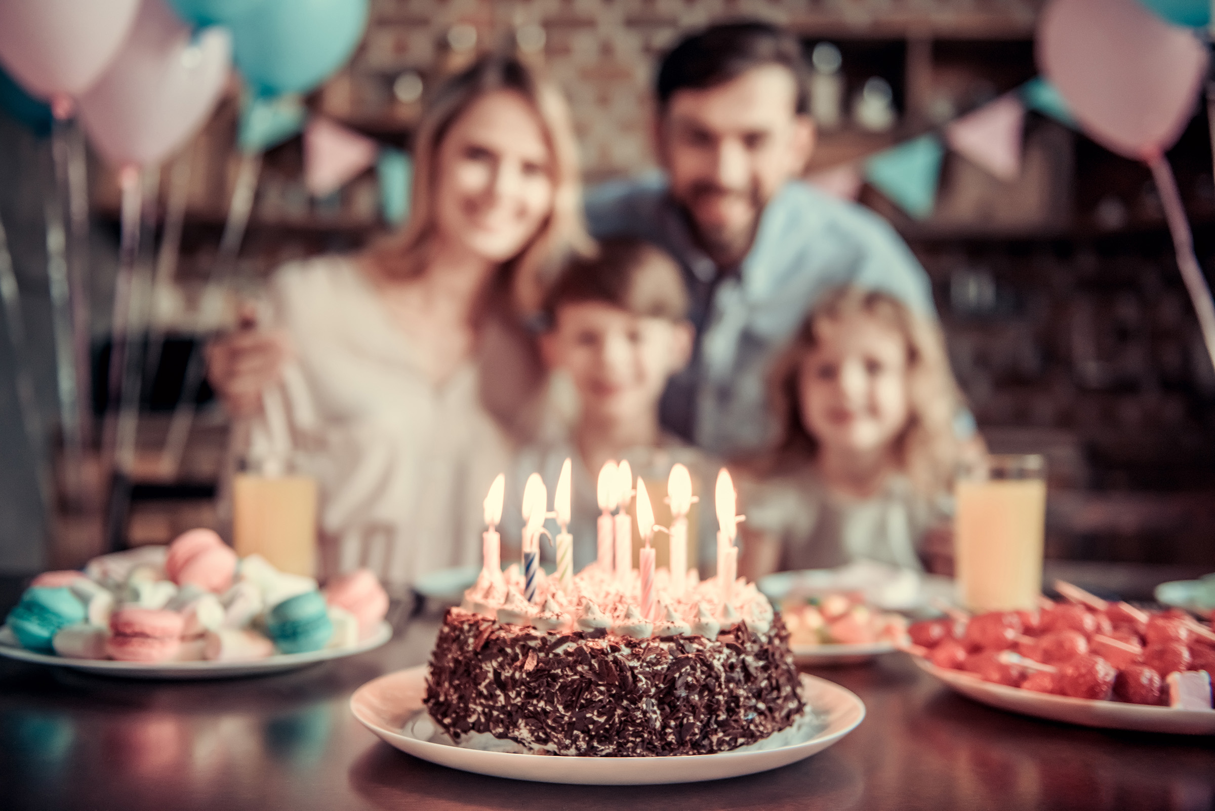 Happy family is sitting at the table in decorated kitchen during birthday celebration, birthday cake in the foreground.