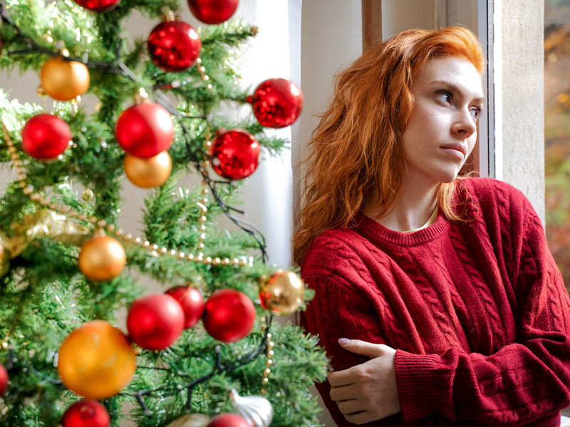 Women staring out of a window next to a decorated Christmas tree.