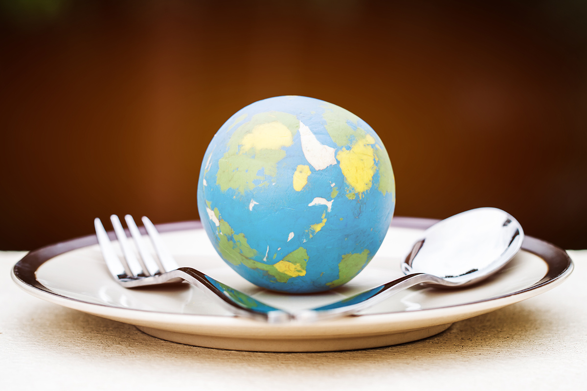 globe on a plate with a four prong fork on the left and a spoon on the right.