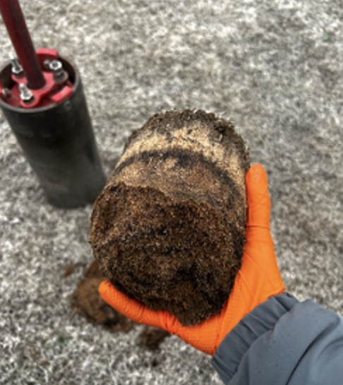 A person wearing an orange glove as they hold compacted dirt.