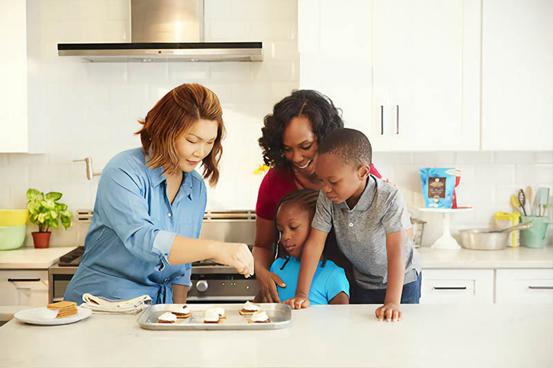 Two women and two kids cooking together in a kitchen.