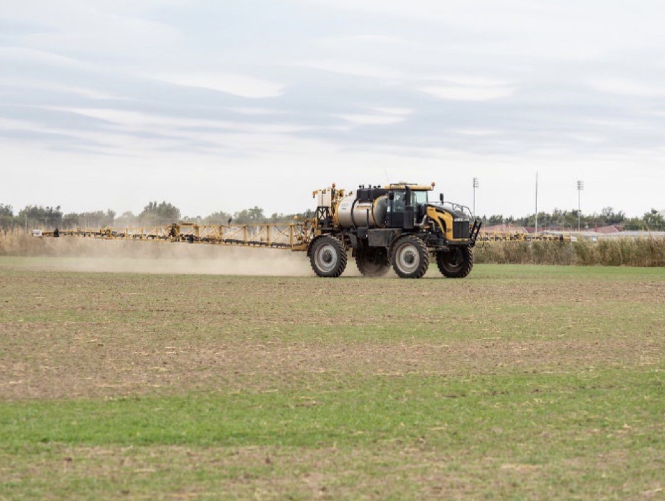 A yellow tractor driving through a field of grass. 