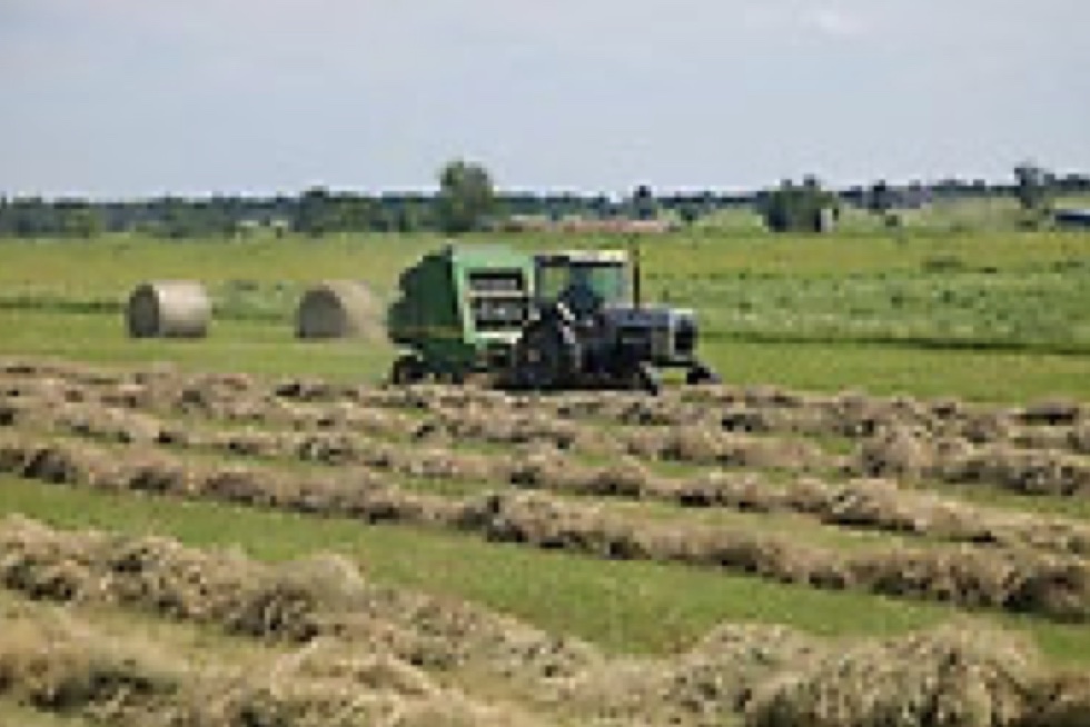 A tractor in the middle of a grass field with hay bails. 