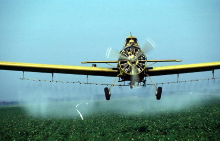 An airplane dropping pesticides on a field.