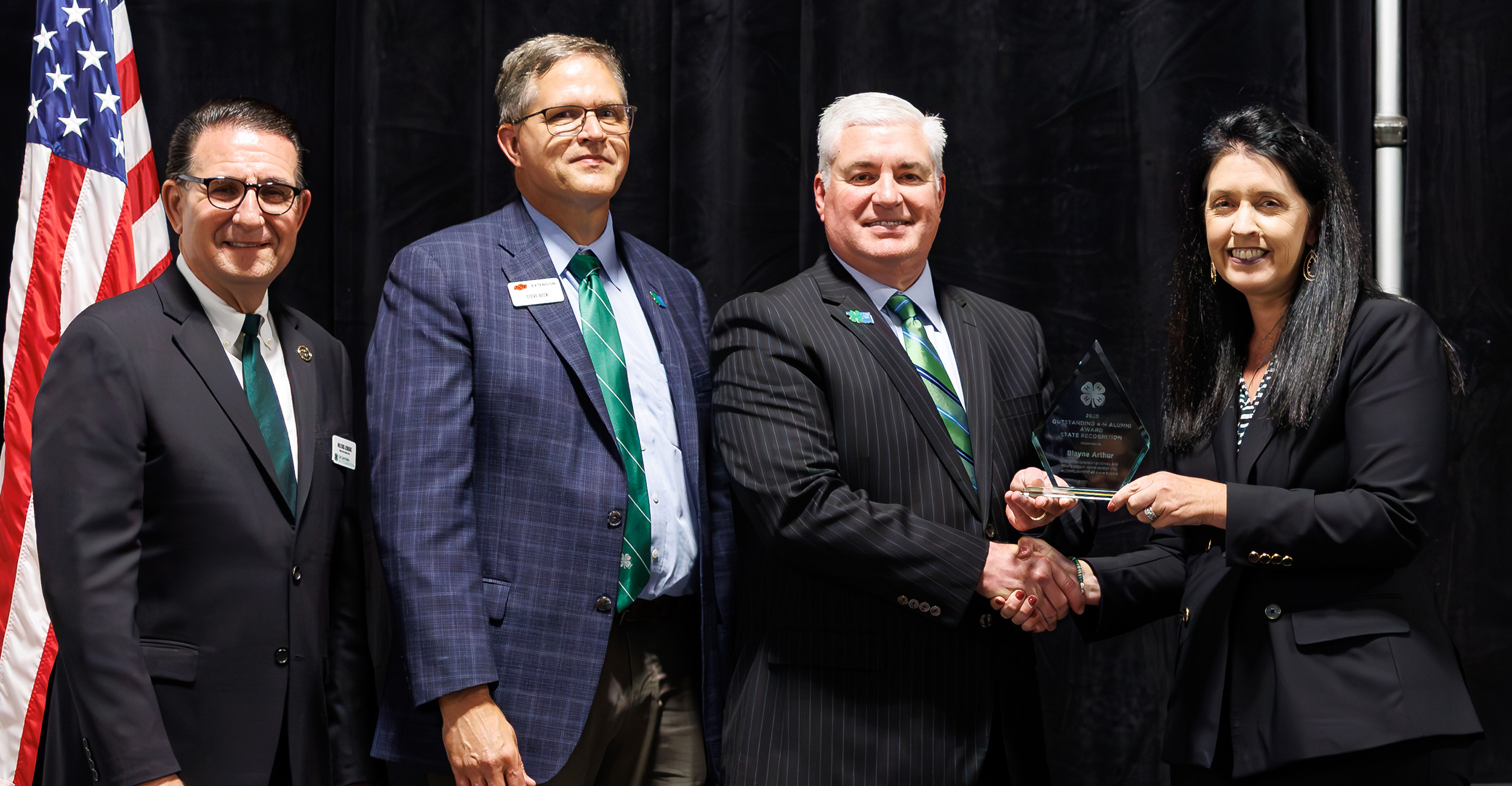 Milford Jenkins, Steve Beck, Jerry Kiefer and Blayne Arthur stand in front of a black background with an American flag in the left corner.
