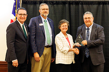 Dr. Randy Harp holds the 2026 Outstanding 4-H Alumni Award on stage with Milford Jenkins, Steve Beck and Gaye Pfeiffer.
