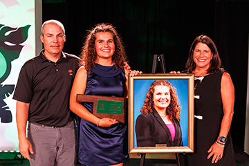 2026 Oklahoma 4-H Hall of Fame inductee Dani McTague stands with a plaque and her framed portrait between her parents.