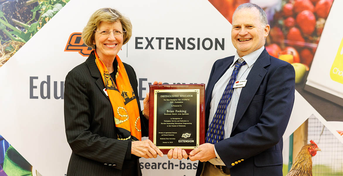 Damona Doye in a black blazer and orange scarf awards Brian Freking with a plaque. He's wearing a blue and yellow tie, white shirt and blue suit coat.