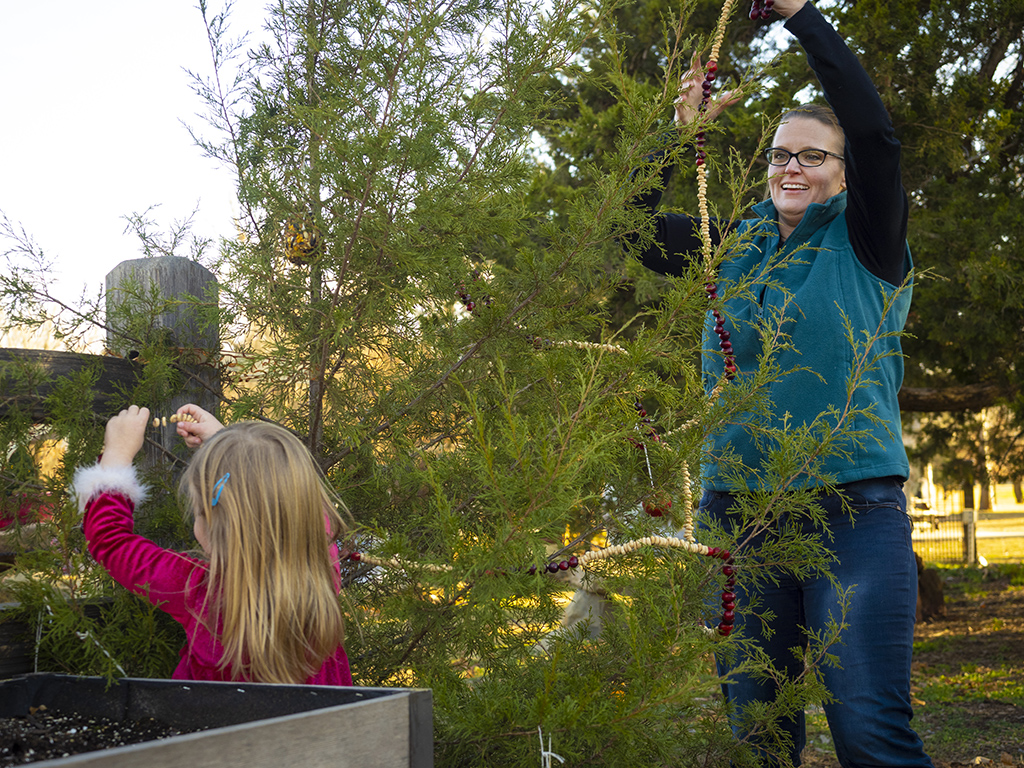 woman and girl hanging cranberry and cereal garland on tree