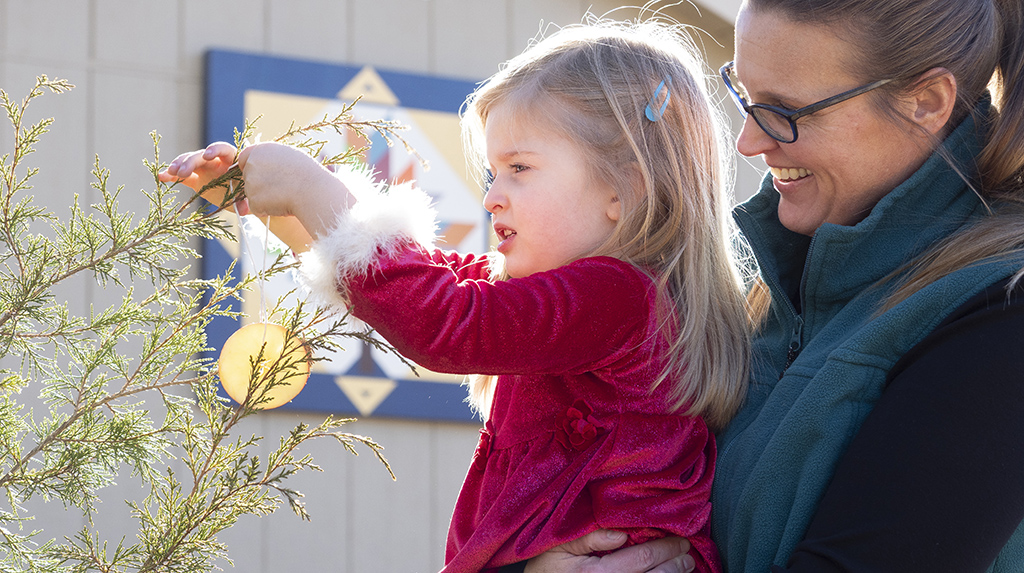woman and girl hanging orange slice ornament on tree