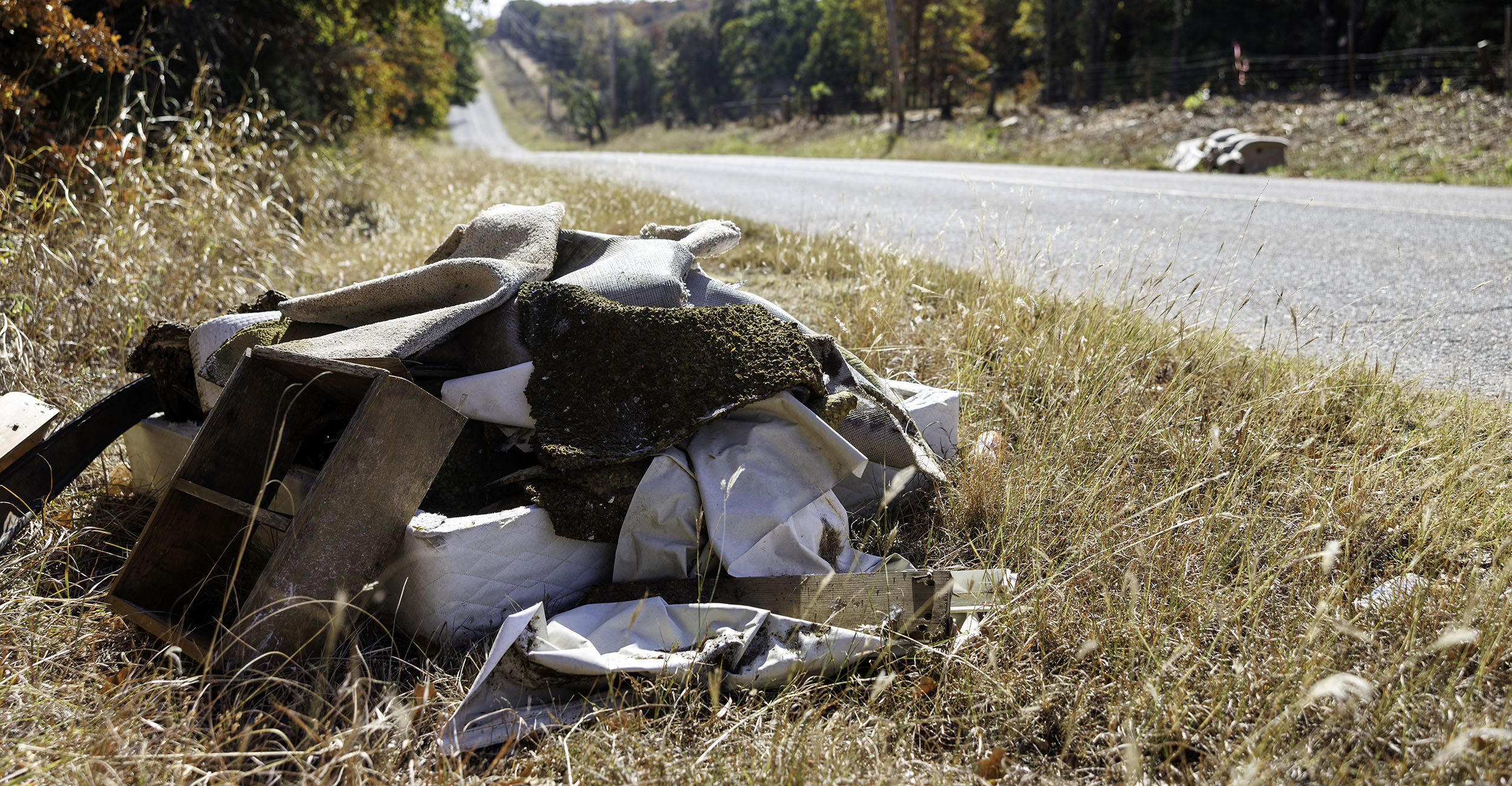 Old mattress, used carpeting and a wooden box dumped illegally alongside a rural road.