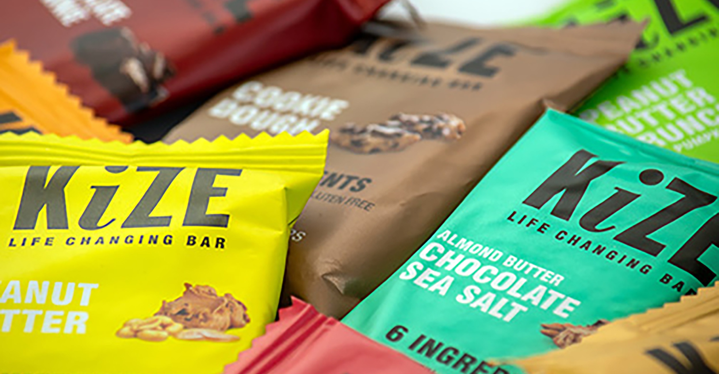 Various flavors of KiZE energy bars in different colored packages.