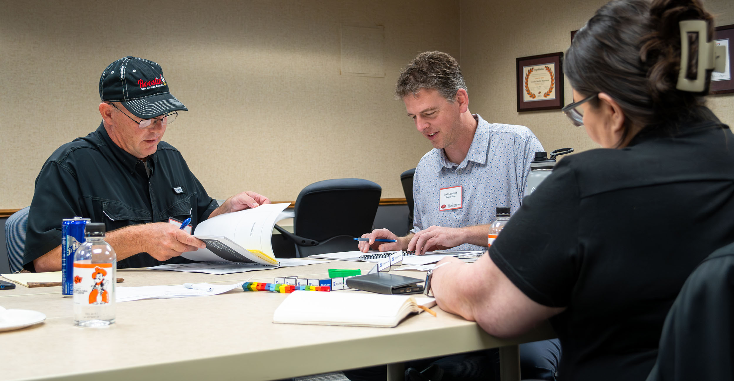 Three people, two men and one woman, sit at a table as they read workshop material.