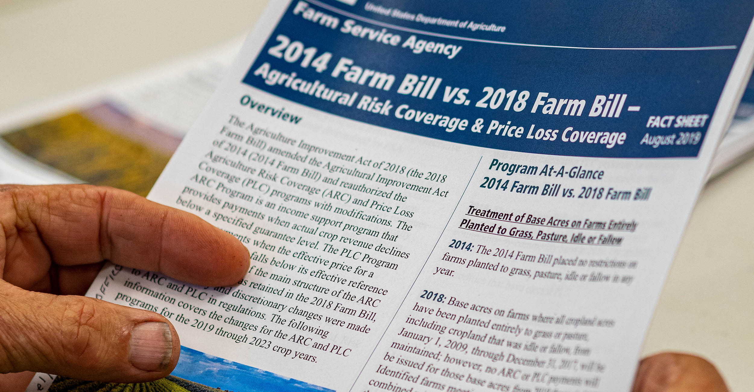 A man's hands hold a piece of paper that says 2014 Farm Bill vs. 2018 Farm Bill.