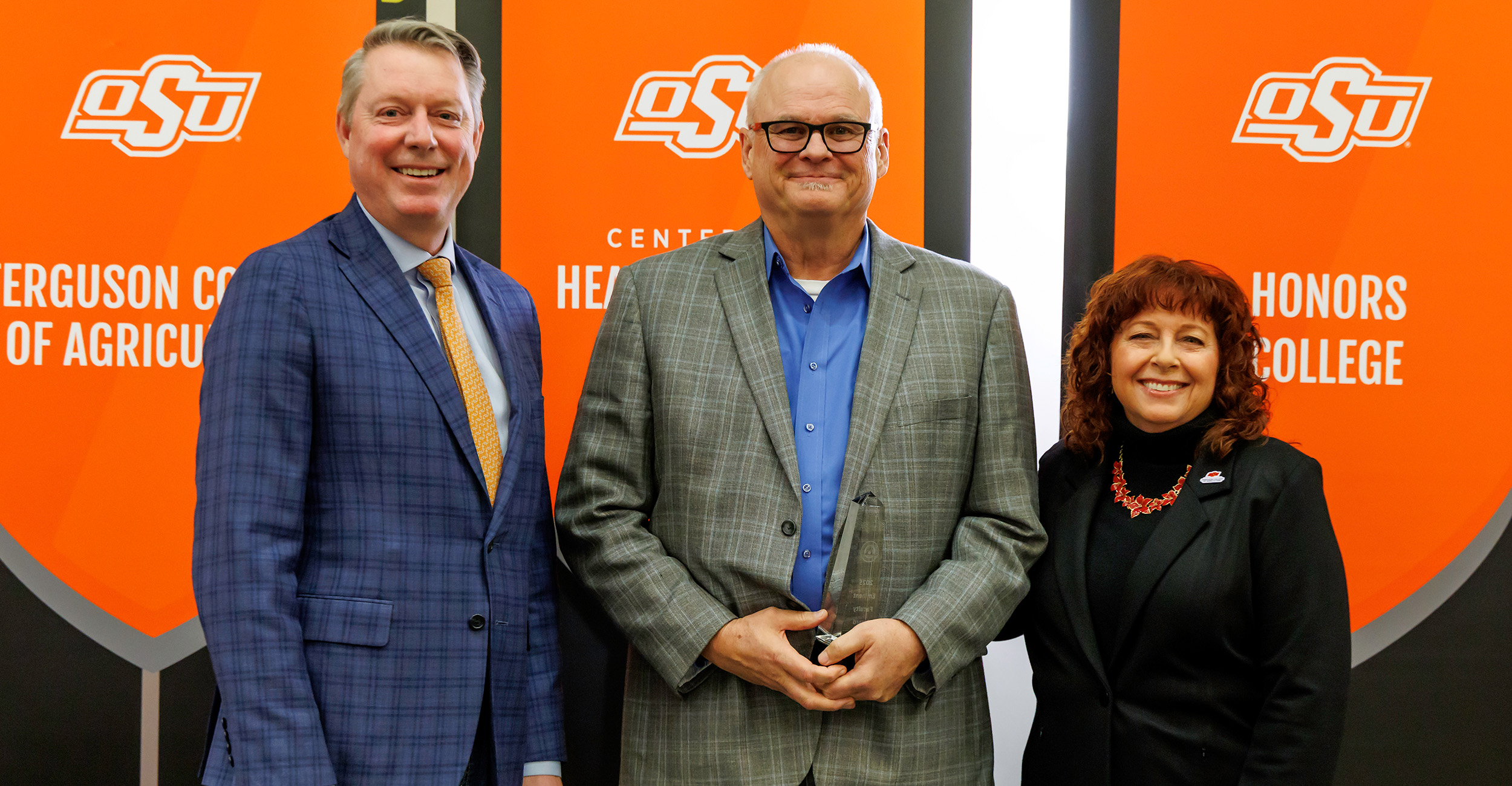 Sam Fuhlendorf stands between Jayson Lusk, vice president and dean of OSU Agriculture and Cynda Clary, associate dean of academic programs, after receiving the OSU Eminent Faculty Award. Fuhlendorf wears a gray suit and stands in front of an OSU backdrop.