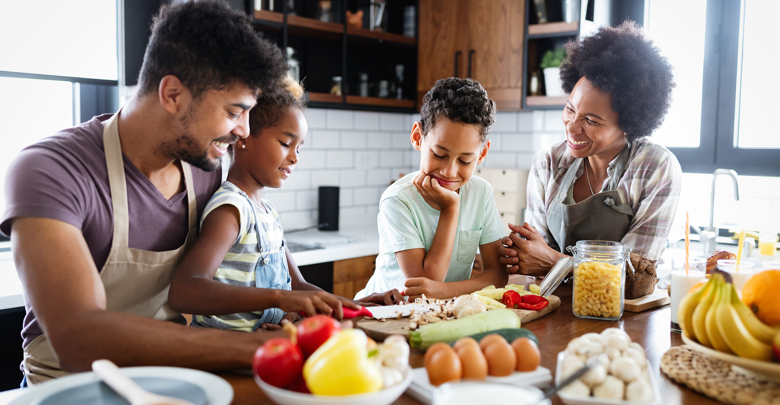 A family of four, consisting of two parents and two children, sit together in a kitchen to prepare a healthy meal.