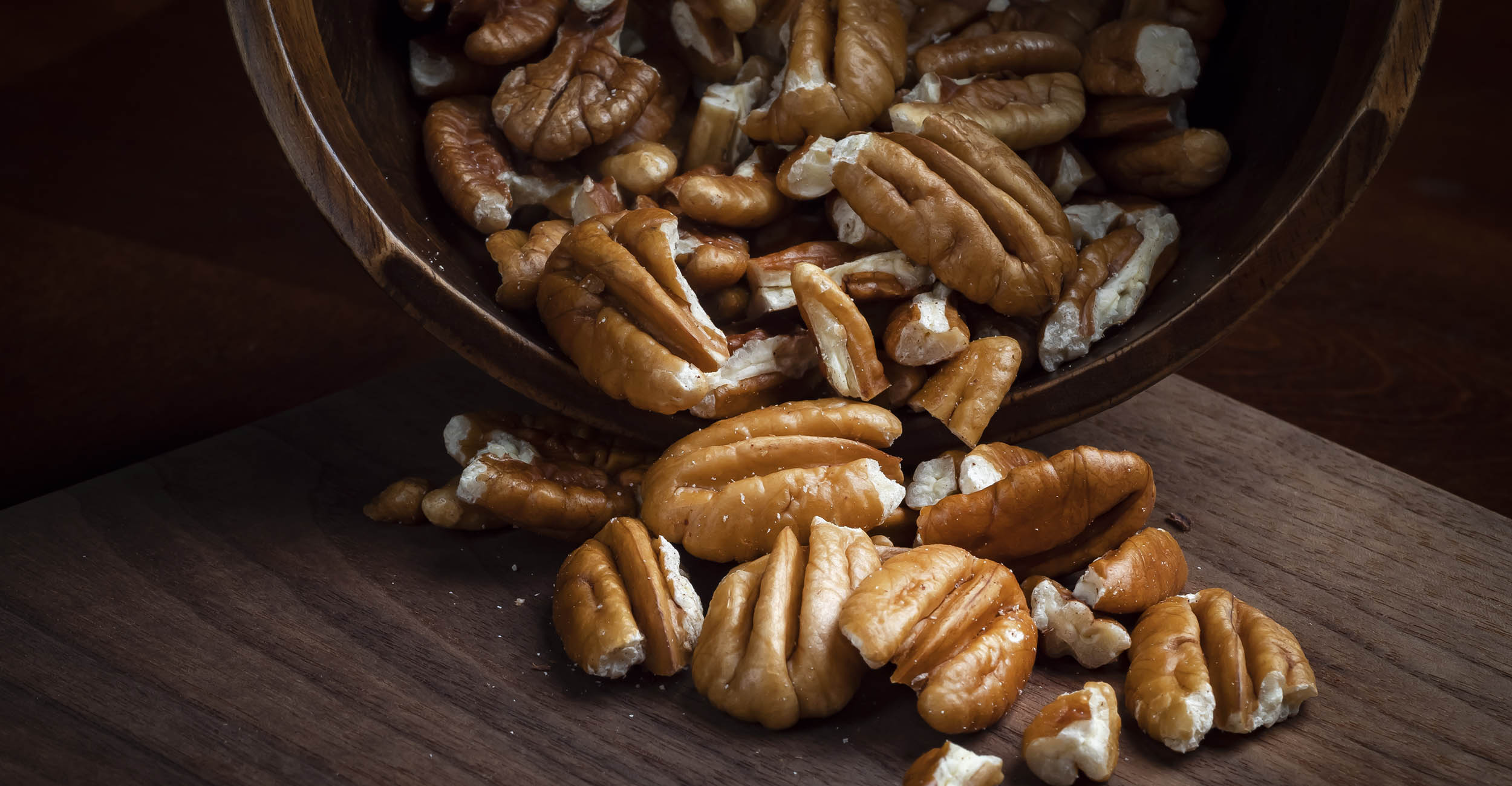 a wooden bowl with shelled and halved pecans spilling out of it