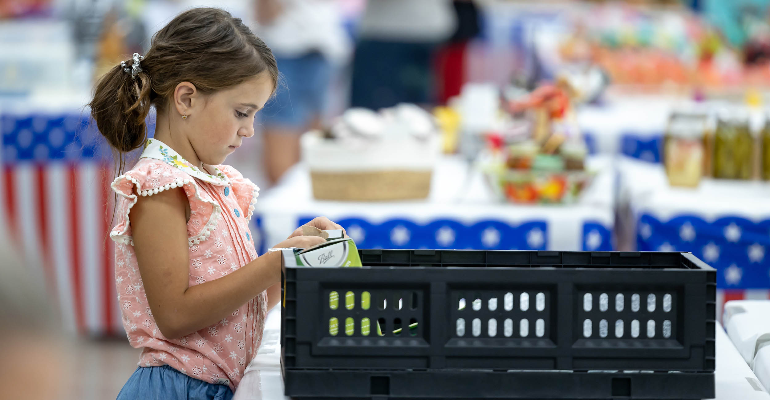 a young girl with brown hair in a ponytail and wearing a pink and white shirt looks at a plastic bin of canning supplies during a Family and Consumer Sciences exhibit during Oklahoma's Lincoln County Fair