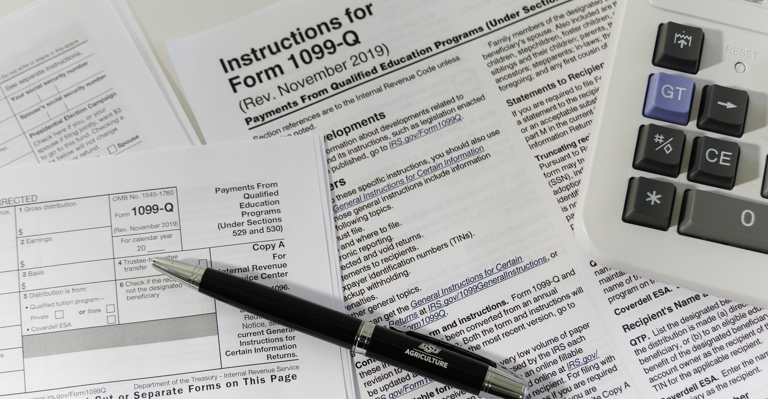 Various tax forms on a table with an ink pen and a calculator.