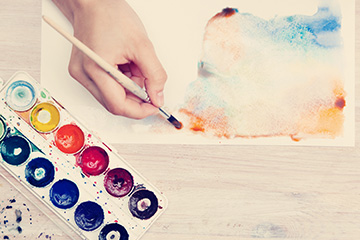 A tray of watercolor paints with a hand holding a paint brush.