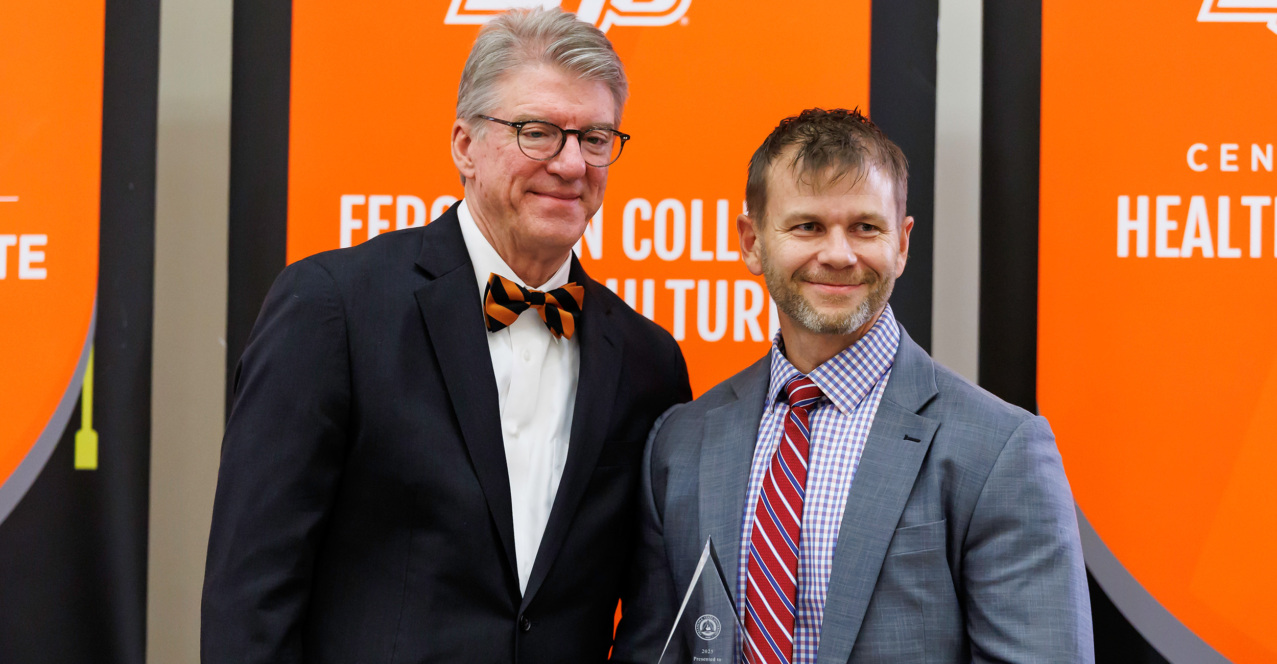 Brian Whitacre (right) poses for a picture with OSU president Jim Hess (left). Whitacre and Hess are both wearing suits, and Whitacre is holding his award.