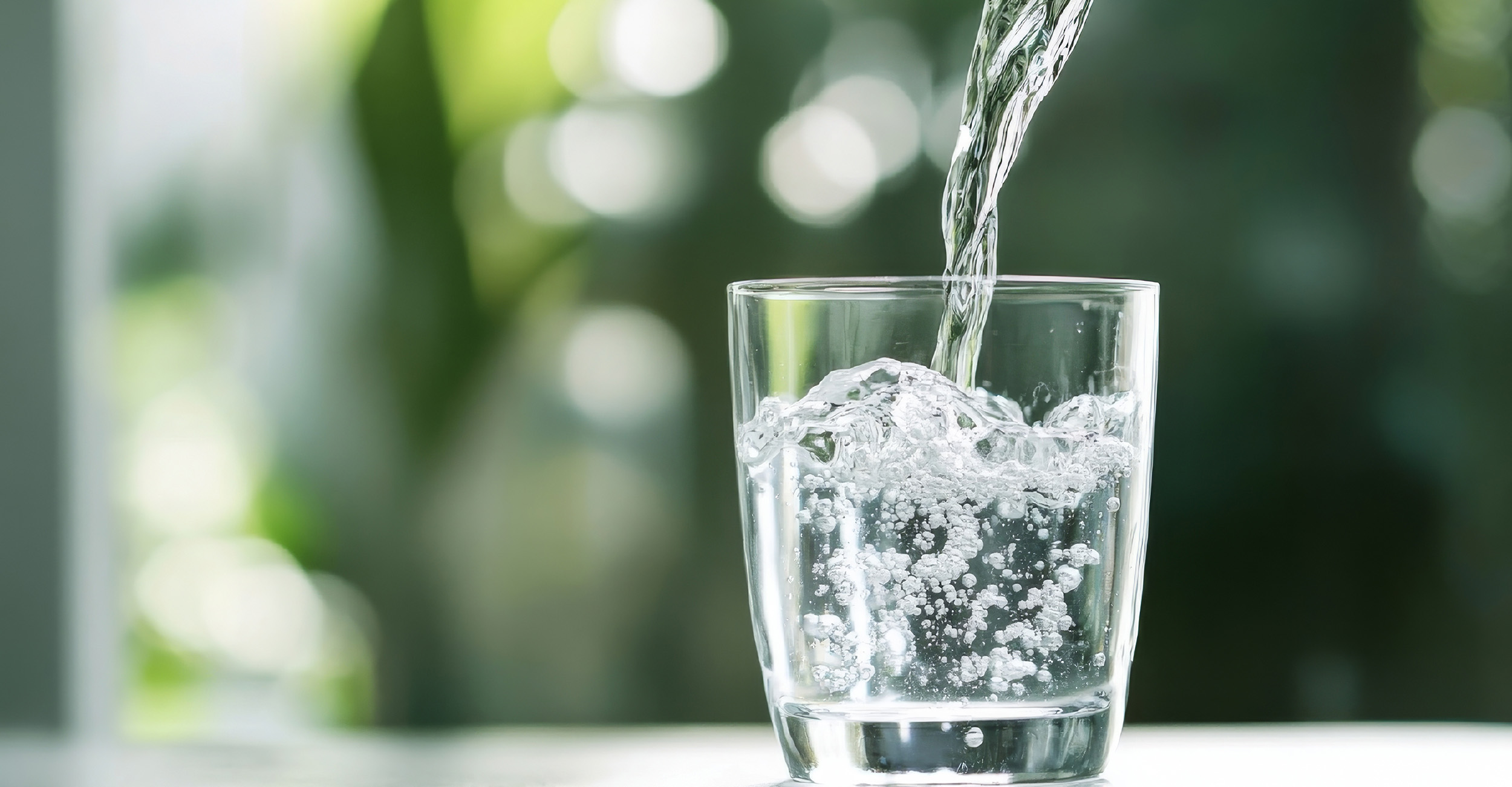 A clear glass on a table being filled with water.