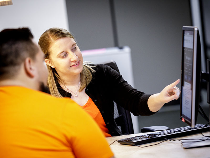 A woman pointing to a computer screen to show something.