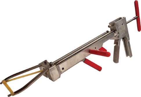 The tool is long and made of silver metal, with several red grip handles along the frame. At one end, there is a mechanism holding a stretched rubber band, while the opposite end has a handle and trigger-like grip used to operate the device.