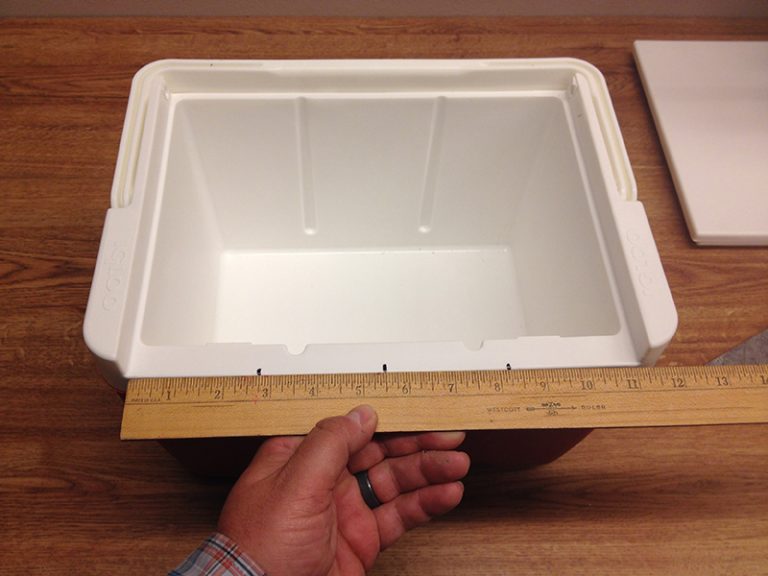 A cooler without a lid being measured with a wooden ruler.