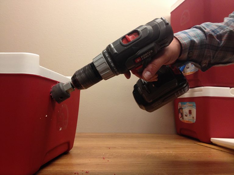A person drilling the side of a red cooler.