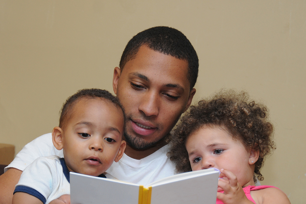 A father reading a book to his young son and daughter.