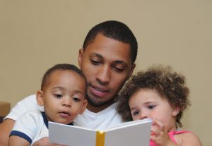 A father reading a book to his young son and daughter.