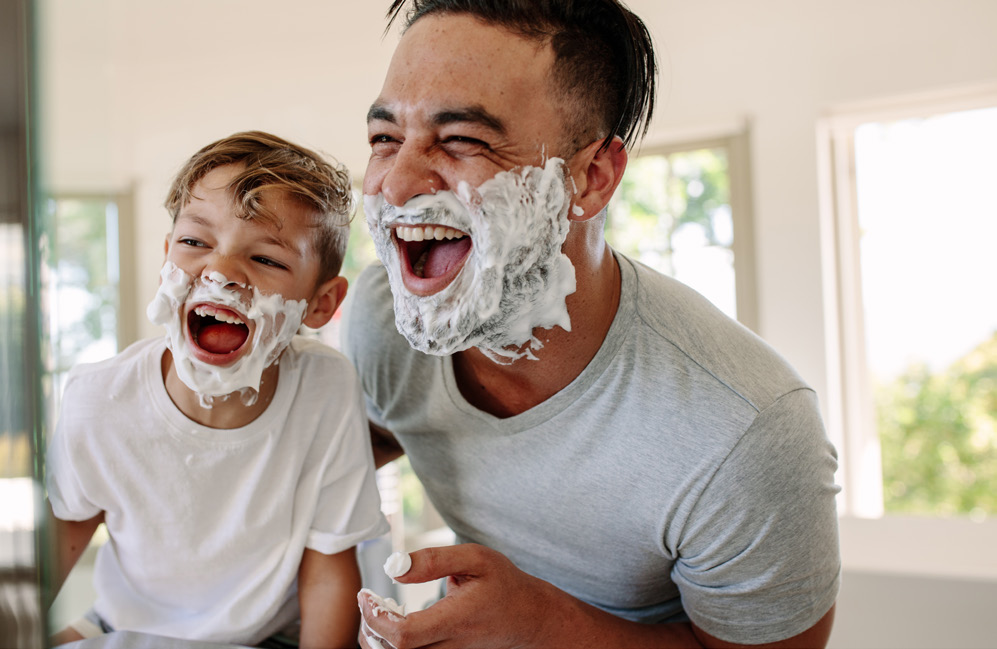 A kid with his dad having shaving cream in their face and laughing.