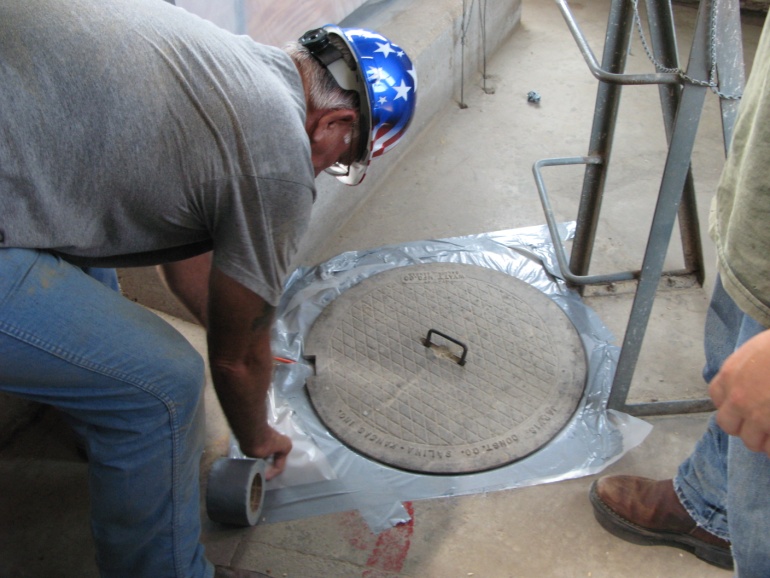 Man sealing manhole cover with polyethylene film