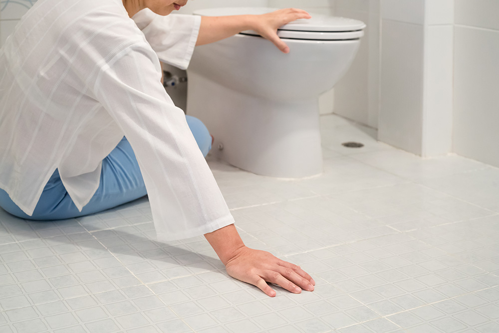 A woman laying on the ground holding her hand on the toilet.