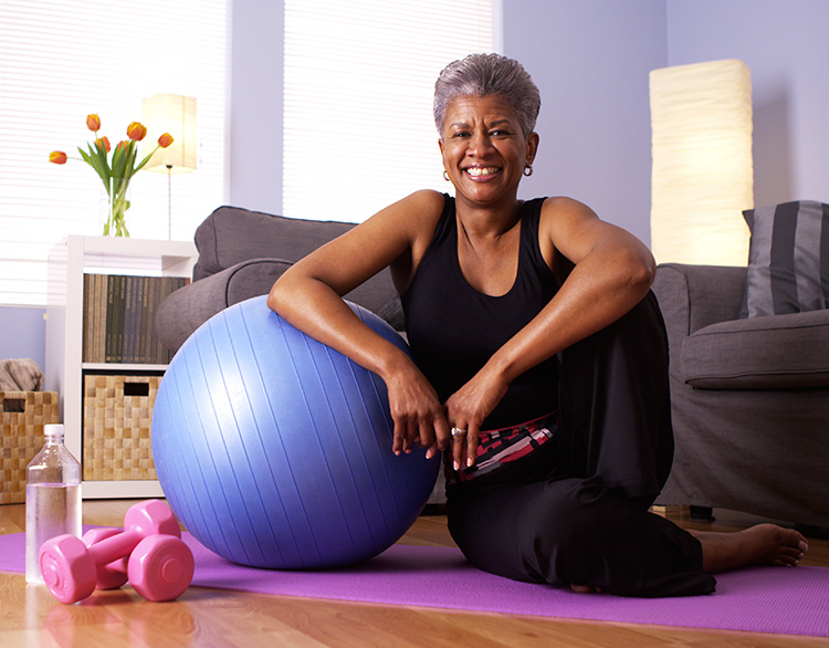Woman smiling as she sits on the floor with workout equipment.