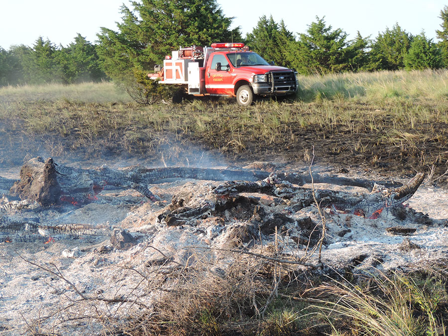 Red fire truck is next to a burn pile.