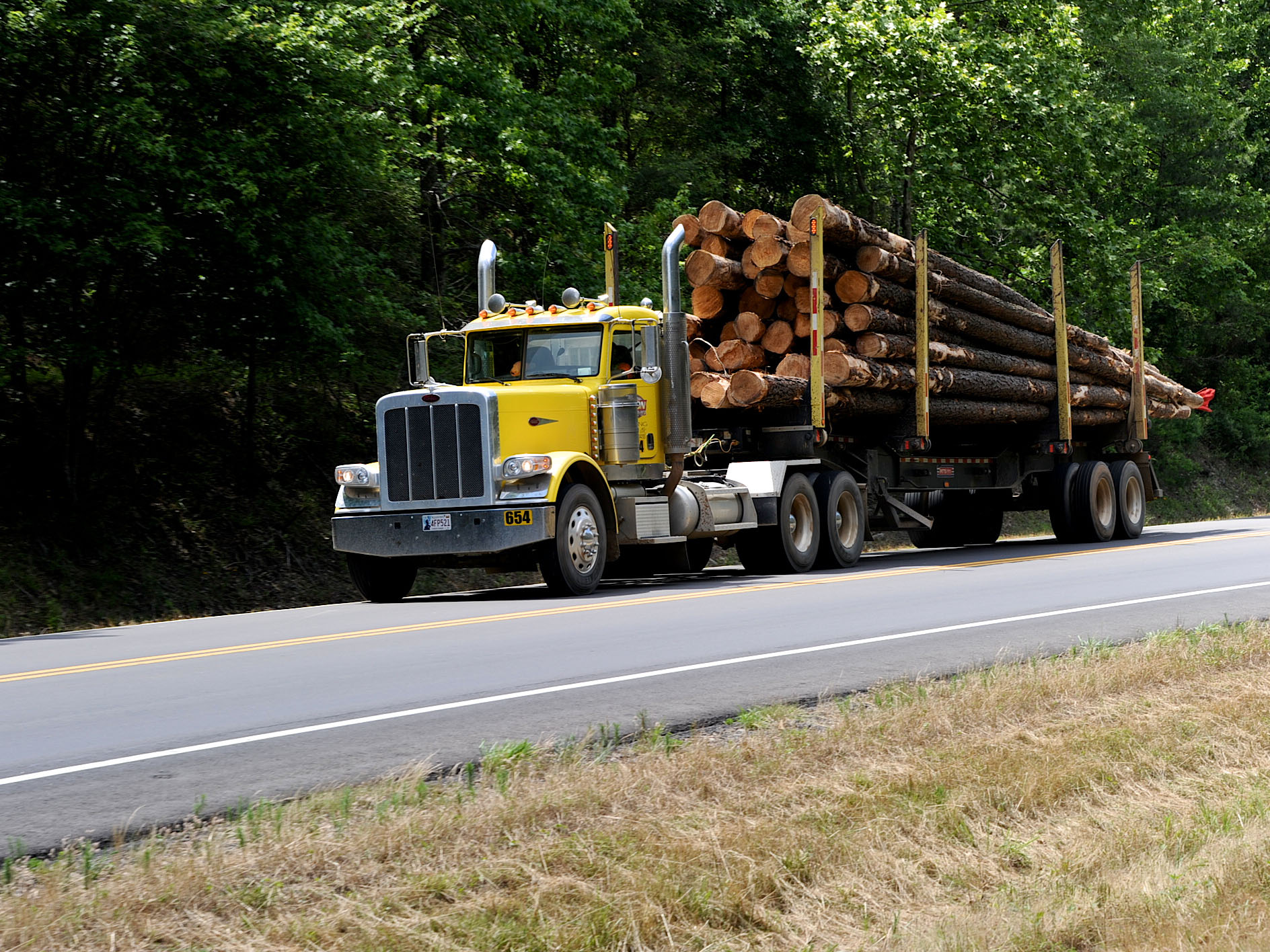 A truck carrying wood logs. A yellow semi truck carrying wood logs driving down a blacktop road.