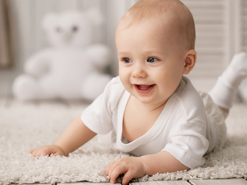 A baby laughing laying on its stomach in a room.