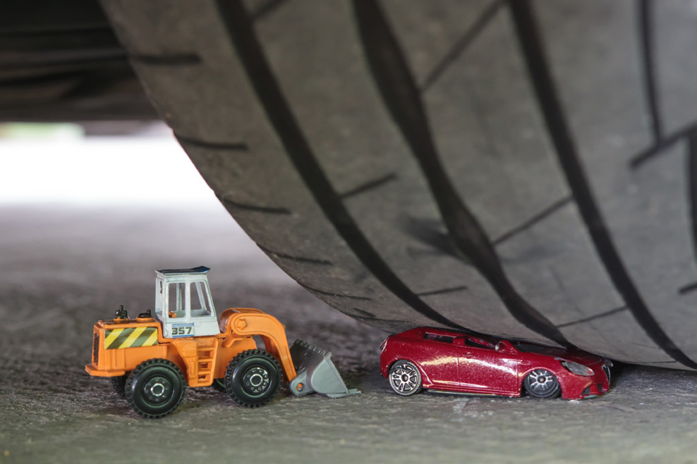 A toy car tries to rescue another toy car that is smashed by an actual tire.