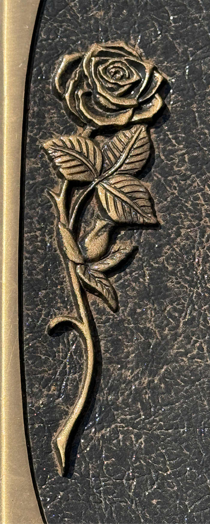 Close-up of engraved rose on bronze grave marker, detailed floral design on textured surface symbolizing remembrance and memorial tribute.