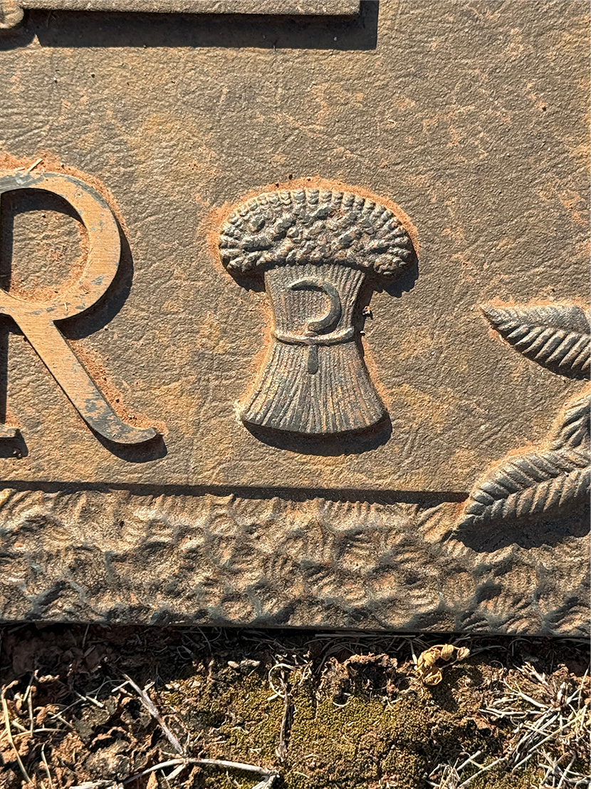 Close-up of carved sheaf of wheat on weathered stone gravestone.