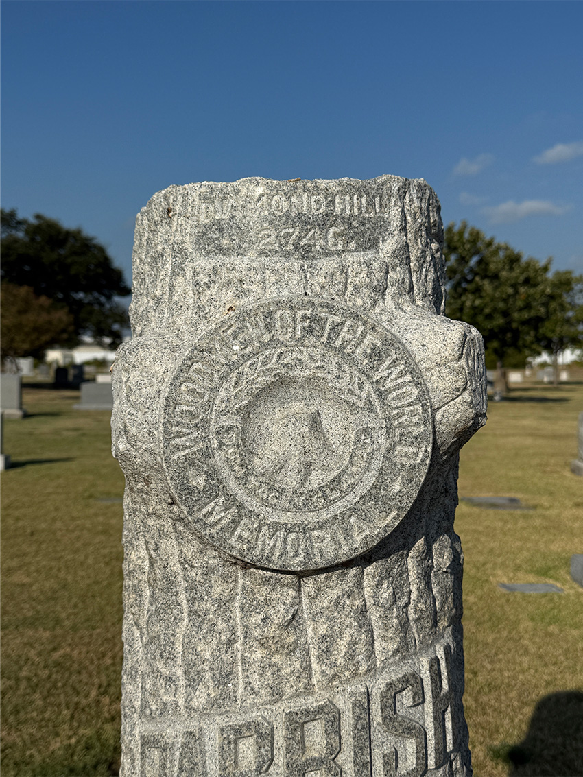 Close-up of a weathered tree stone grave marker with a circular Woodmen of the World symbol.