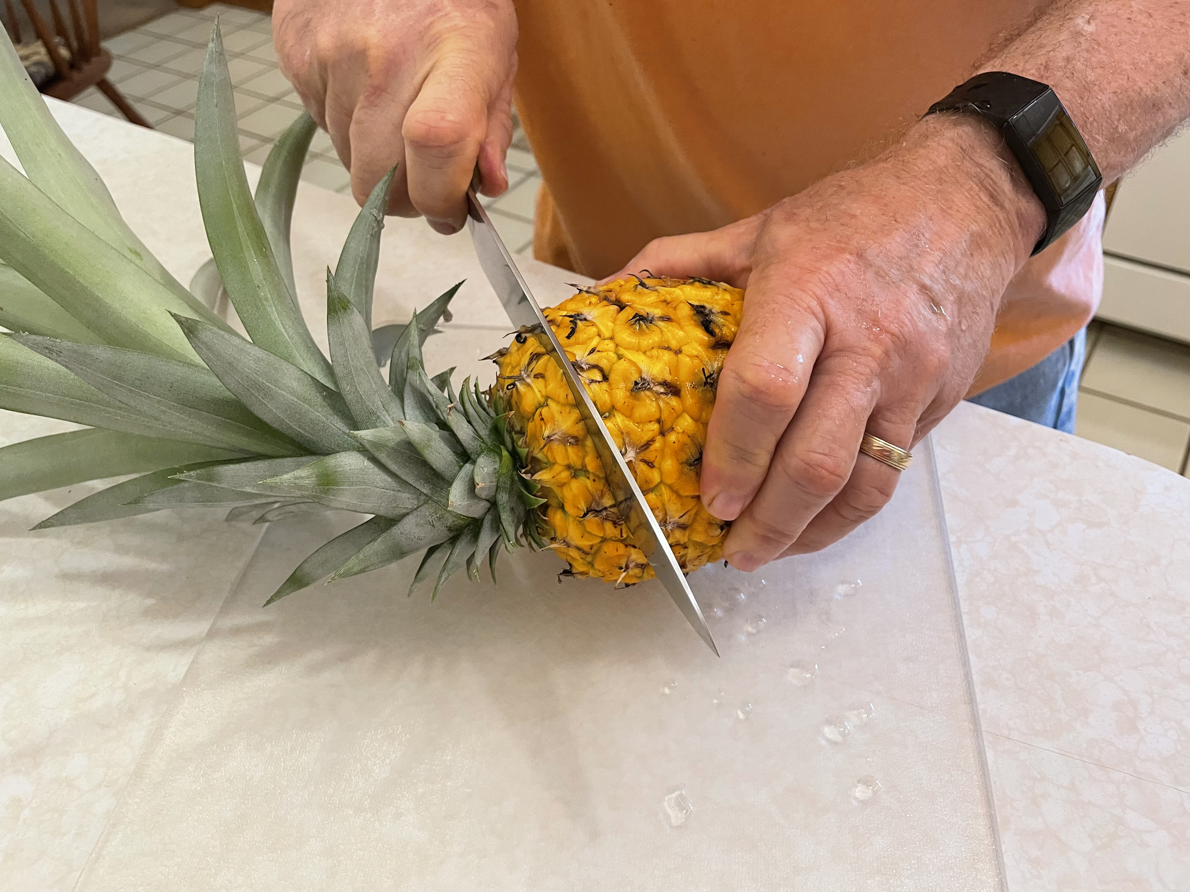 A person using a sharp knife to cut the top of a pineapple.